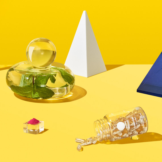 Ritual Essential for Women bottle shown in a yellow staged background with mint leaves and other props scatted around