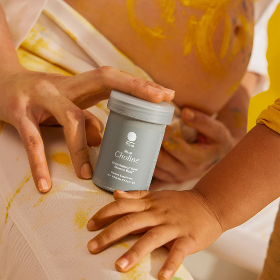A model holding the Natal Choline bottle near her leg with a child's hand resting near it