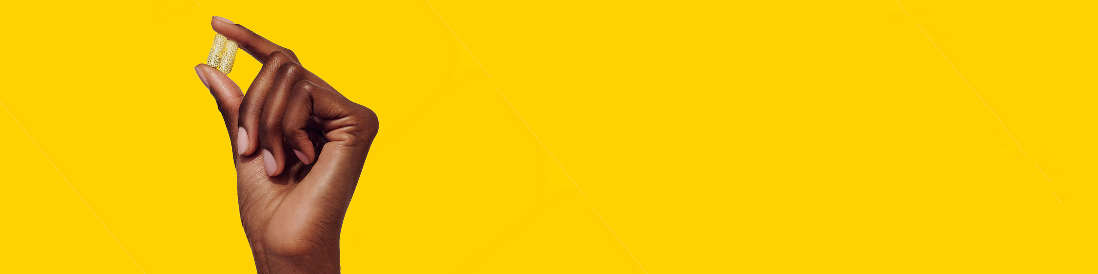 Two vitamin capsules being held between two fingers on a yellow background.